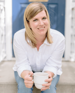 Kara from blue_alice_space_design sitting on a doorstep with a white shirt and jeans, and white coffee cup