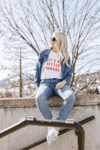 Carly Mal Trendsetter sitting on cement wall with Denim jeans and jacket