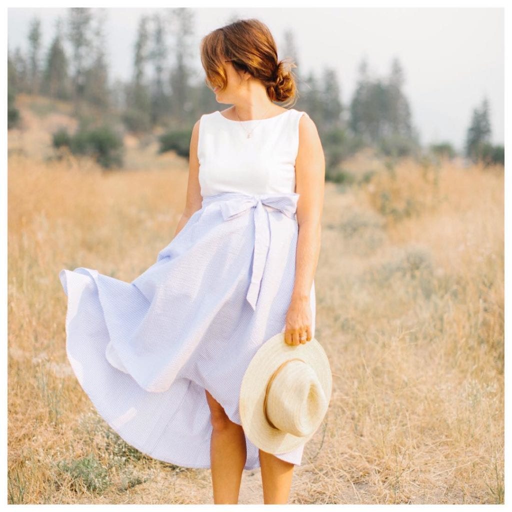 Jillian Harris (@Jillian.Harris) is a fashion influencer and TV star from Vancouver, here she is wearing a pale blue sundress with a beige hat in a Kelowna field with trees behind