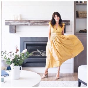 Jillian Harris (@Jillian.Harris) is a fashion influencer and TV star from Vancouver, here she is wearing a bright yellow sundress standing in front of a while brick fireplace in a modern interior