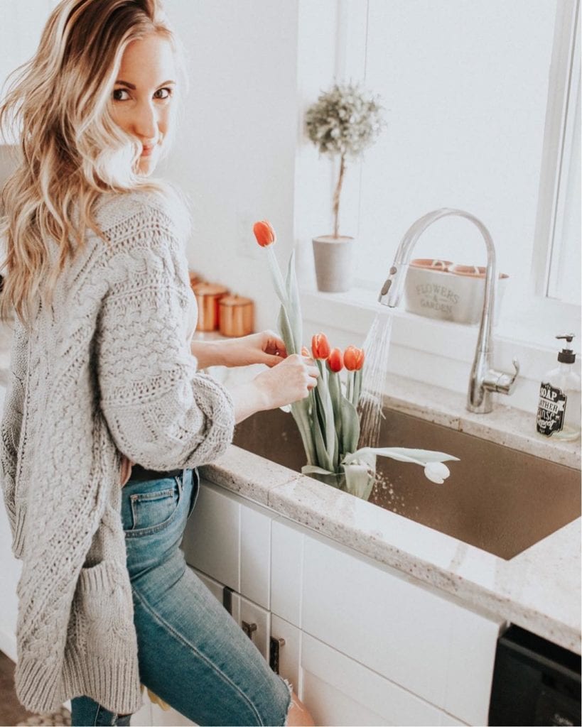 Stesha (@stesharose), family and fashion blogger and trend setter, organizing tulips in a vase in her kitchen sink, wearing a cozy sweater and jeans