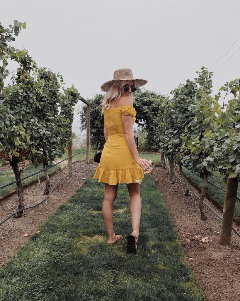 Tessa (@tessalindsaygarcia) is a fashion blogger from Vancouver that frequents the Okanagan; here she wearing a yellow sundress and a beige hat, standing in an orchard